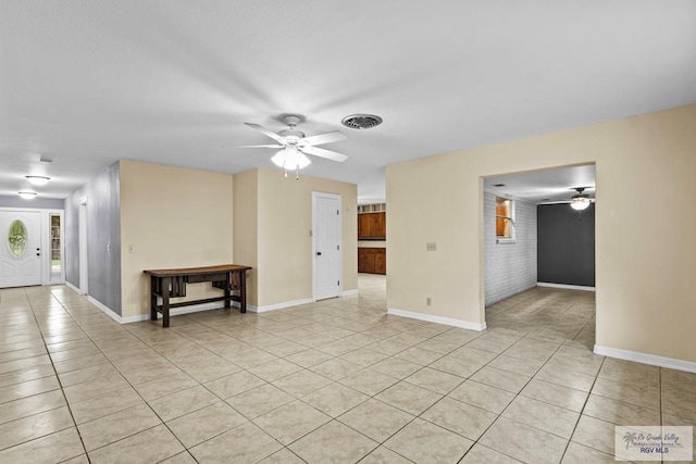 tiled spare room with ceiling fan and brick wall