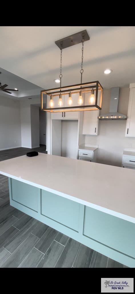kitchen with a ceiling fan, wood tiled floor, recessed lighting, wall chimney range hood, and decorative light fixtures
