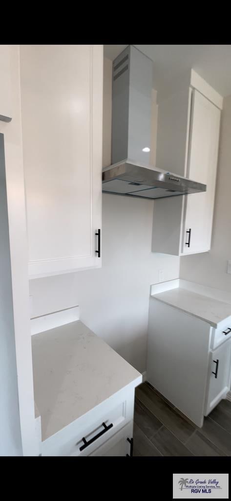 interior space with white cabinetry and wall chimney range hood
