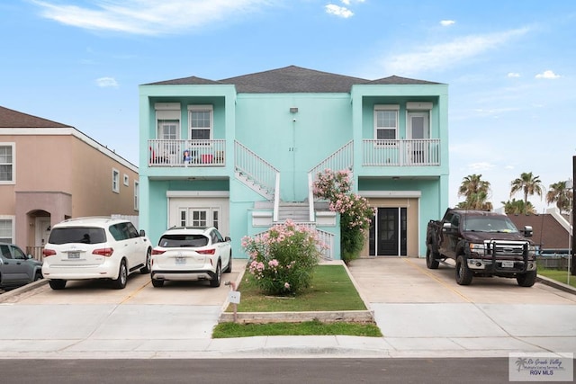 110 E Retama St, South Padre Island, TX 78597 - view of front facade featuring stucco siding, stairs, roof with shingles, and driveway