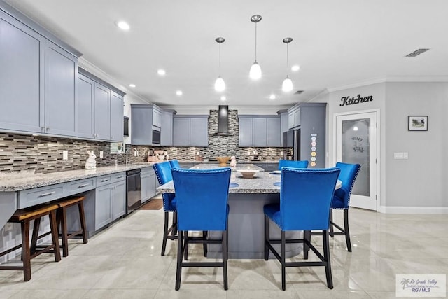 kitchen featuring wall chimney exhaust hood, visible vents, a kitchen island, dishwasher, and a kitchen bar