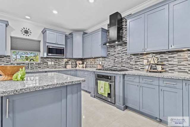 kitchen featuring wall chimney exhaust hood, gray cabinets, stainless steel appliances, crown molding, and a sink