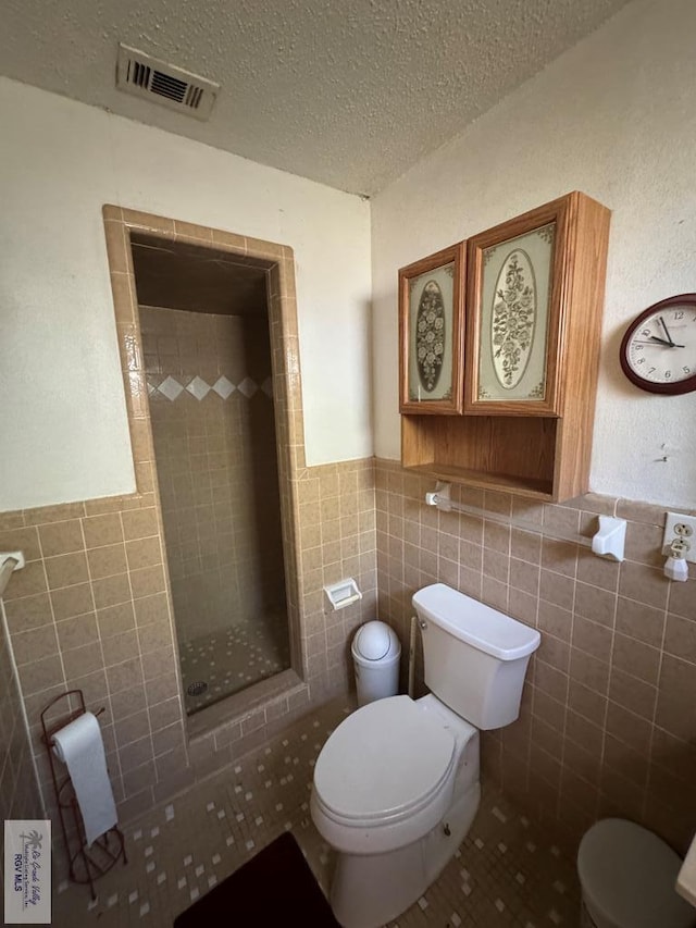 bathroom with a tile shower, a textured ceiling, toilet, and tile walls