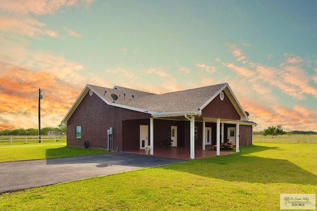 view of front of house featuring aphalt driveway, roof with shingles, a front yard, a patio area, and fence