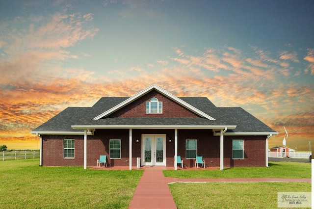 view of front of property with brick siding, a front yard, fence, and french doors