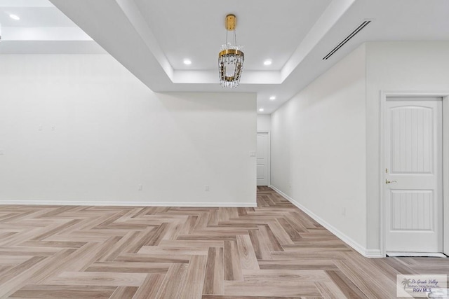 unfurnished room featuring an inviting chandelier, a tray ceiling, and light parquet flooring