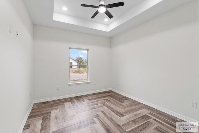 spare room featuring a tray ceiling, parquet flooring, and ceiling fan