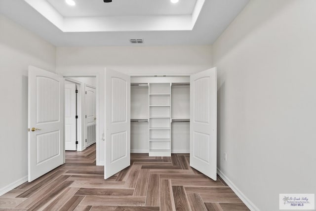 unfurnished bedroom with a tray ceiling, dark parquet flooring, and a closet