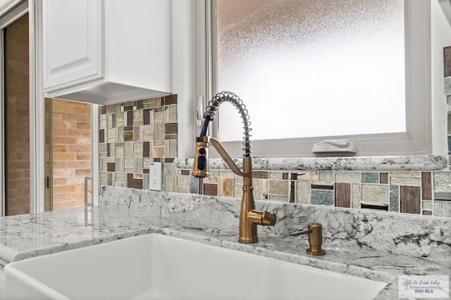 interior details with white cabinetry, sink, and light stone counters