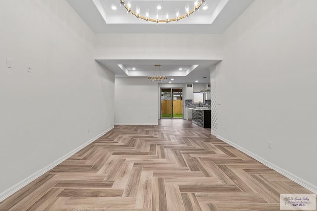 interior space with a tray ceiling, a chandelier, and light parquet floors