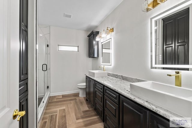 bathroom featuring parquet flooring, vanity, toilet, and a shower with door