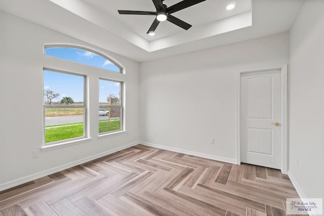 unfurnished room with ceiling fan, light parquet flooring, and a tray ceiling