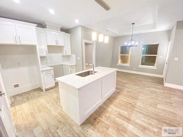 kitchen featuring light wood-style floors, an island with sink, white cabinetry, a sink, and baseboards