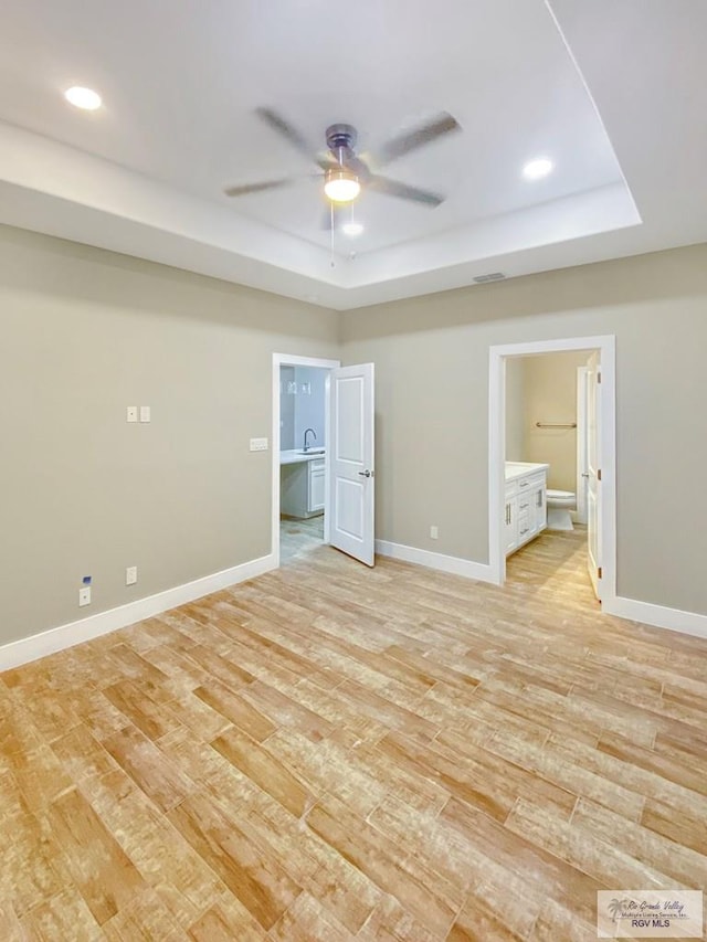 unfurnished bedroom with baseboards, a raised ceiling, recessed lighting, connected bathroom, and light wood finished floors