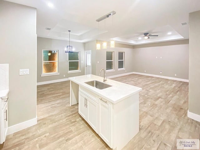 kitchen with baseboards, a sink, open floor plan, a tray ceiling, and ceiling fan with notable chandelier