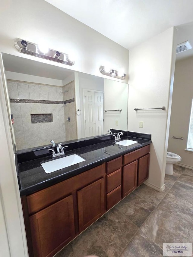 full bath with a sink, tiled shower, toilet, and double vanity