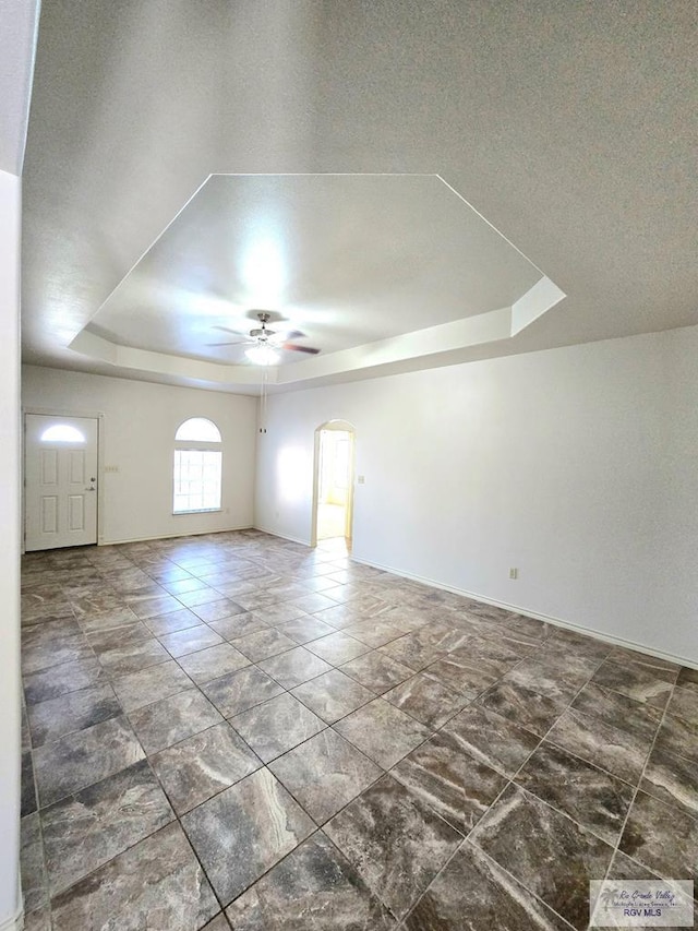 unfurnished room featuring arched walkways, a tray ceiling, a ceiling fan, and baseboards