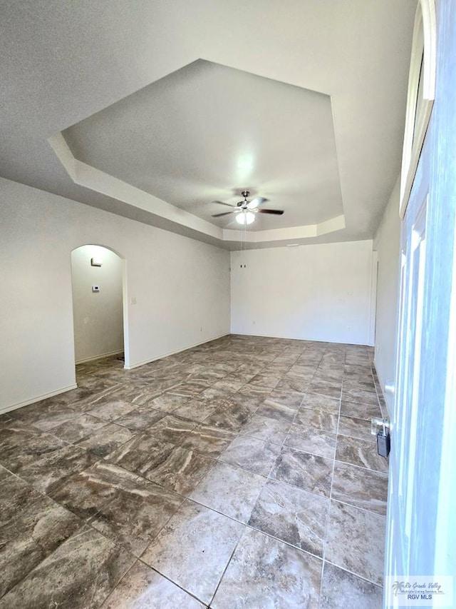 unfurnished room with a ceiling fan, a raised ceiling, and arched walkways