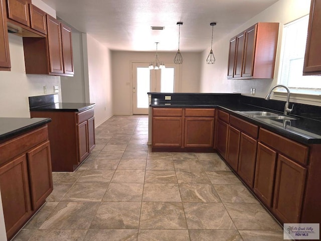 kitchen with visible vents, a peninsula, dark countertops, a chandelier, and a sink
