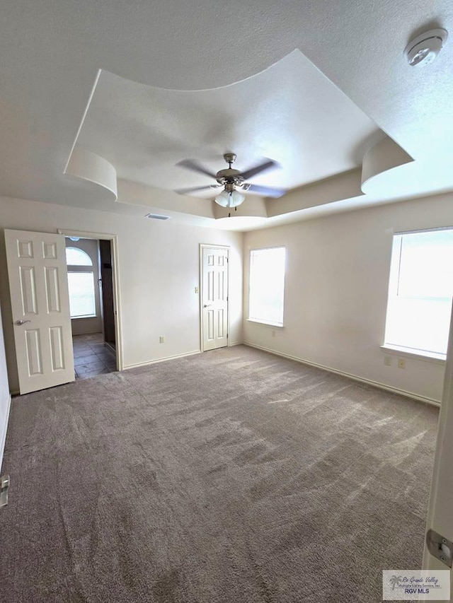 carpeted spare room featuring a ceiling fan, baseboards, and a raised ceiling