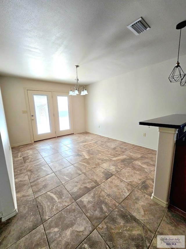 unfurnished dining area with a textured ceiling, baseboards, a notable chandelier, and visible vents
