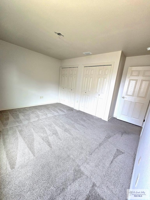 unfurnished bedroom featuring carpet floors, baseboards, two closets, and visible vents