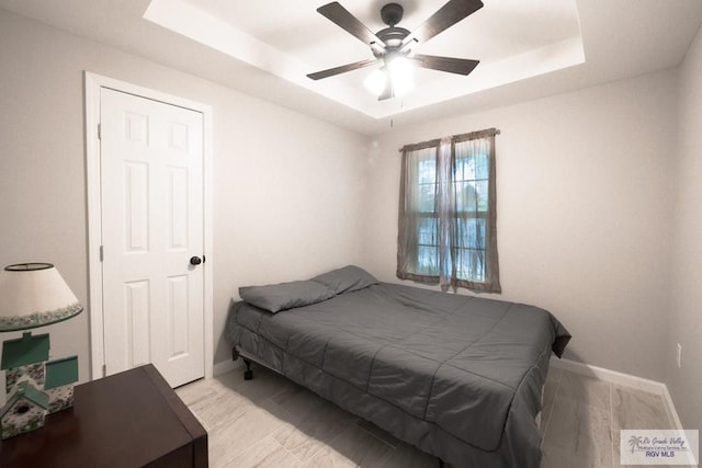 bedroom with a raised ceiling, a ceiling fan, and baseboards