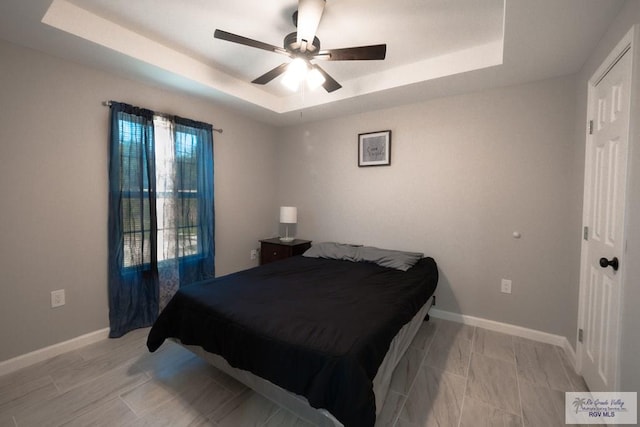 bedroom featuring ceiling fan, baseboards, and a tray ceiling