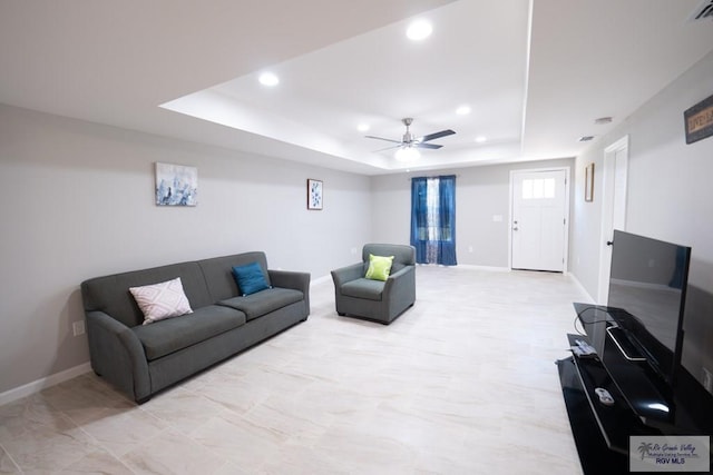 living area with a raised ceiling, recessed lighting, and baseboards