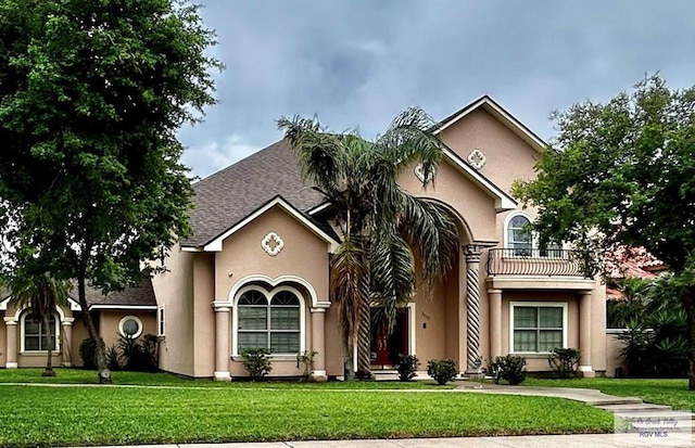 view of front of property featuring a front yard, roof with shingles, a balcony, and stucco siding