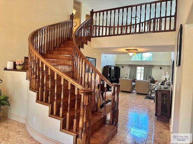 stairway featuring baseboards, marble finish floor, and a high ceiling