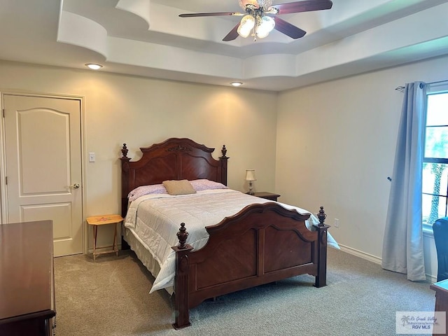 bedroom featuring a tray ceiling, baseboards, a ceiling fan, and light carpet