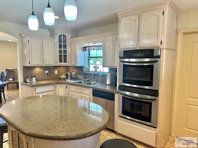kitchen featuring glass insert cabinets, arched walkways, a sink, stainless steel appliances, and decorative backsplash