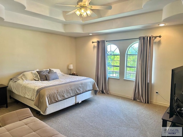 bedroom featuring carpet floors, baseboards, a raised ceiling, and a ceiling fan