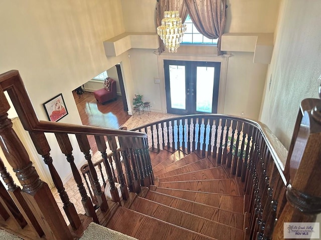 stairs with french doors, an inviting chandelier, a towering ceiling, and baseboards