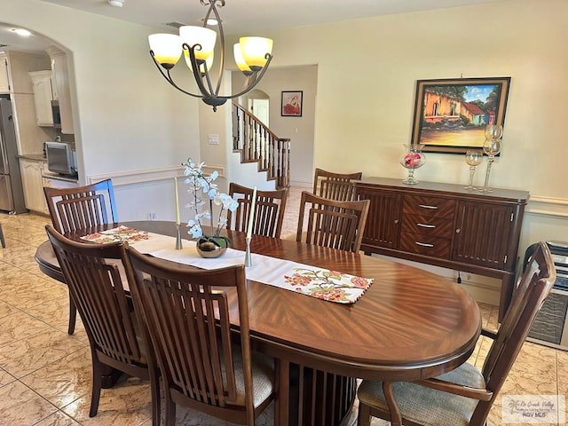 dining space featuring a chandelier, arched walkways, marble finish floor, and a wainscoted wall