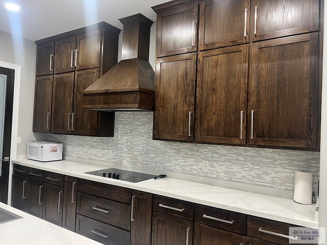 kitchen with black electric cooktop, backsplash, dark brown cabinets, and premium range hood