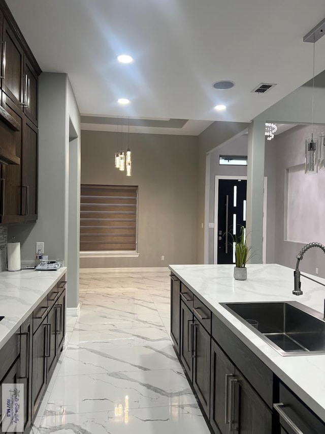 kitchen with black dishwasher, sink, hanging light fixtures, dark brown cabinetry, and light stone counters