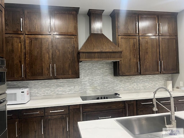 kitchen with premium range hood, dark brown cabinetry, sink, black electric stovetop, and decorative backsplash