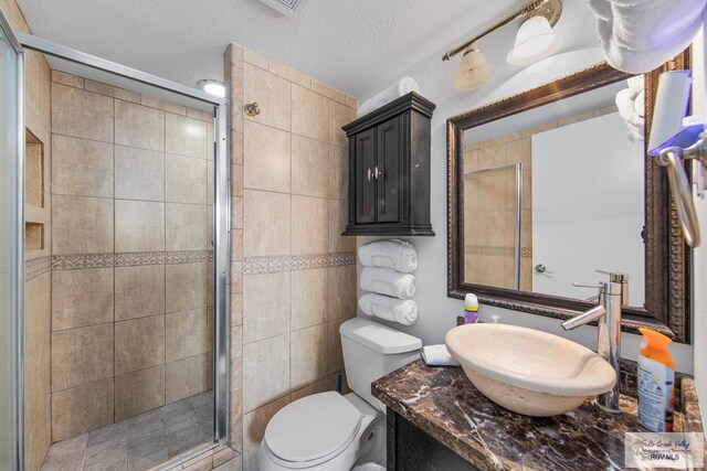 bathroom featuring walk in shower, vanity, a textured ceiling, tile walls, and toilet