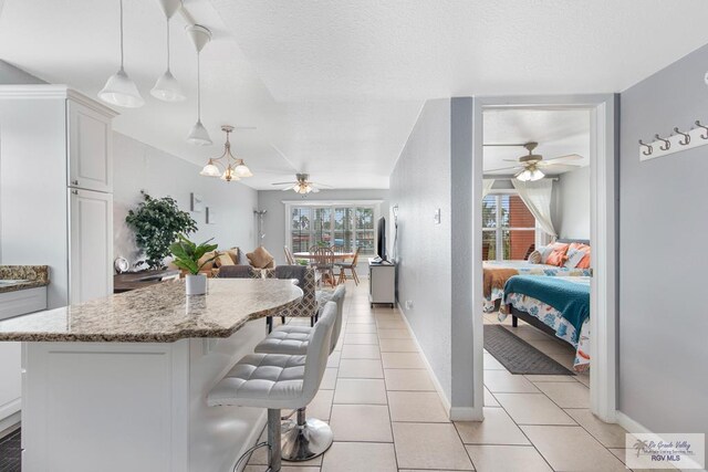 kitchen with white cabinets, pendant lighting, a kitchen bar, light tile patterned flooring, and ceiling fan with notable chandelier