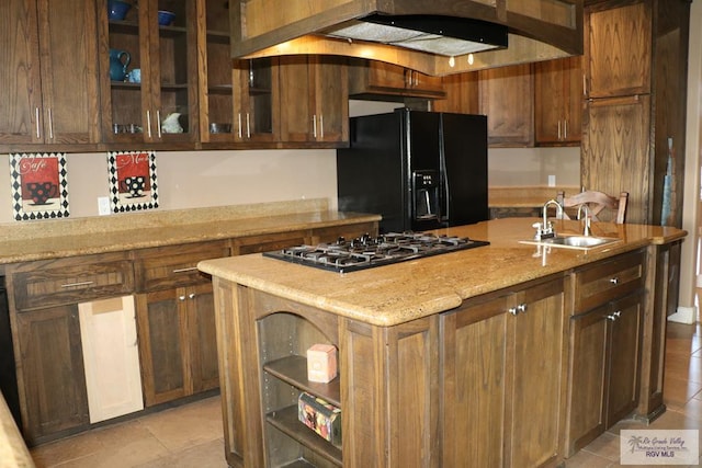 kitchen featuring a kitchen island with sink, black refrigerator with ice dispenser, sink, custom range hood, and stainless steel gas cooktop