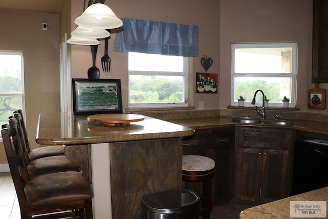 kitchen featuring pendant lighting, dishwasher, sink, dark brown cabinets, and light tile patterned flooring