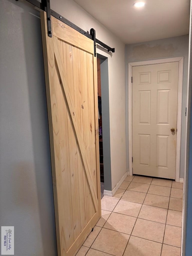 hall featuring baseboards, a barn door, and light tile patterned floors