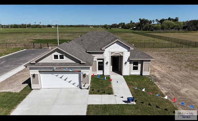 view of front of home featuring a rural view, fence, stone siding, and driveway