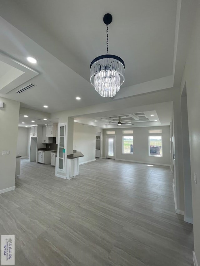 unfurnished living room featuring visible vents, ceiling fan with notable chandelier, baseboards, and a tray ceiling