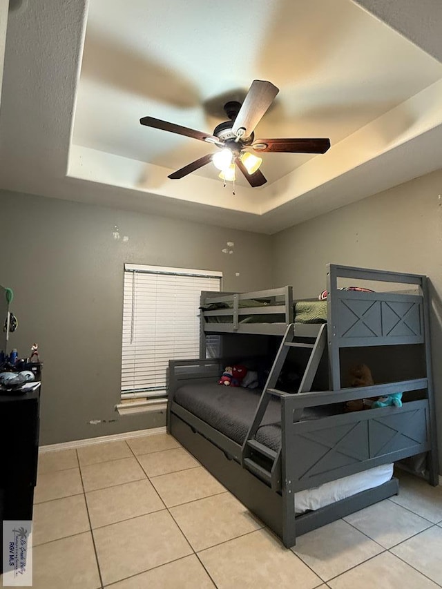 tiled bedroom featuring ceiling fan and a tray ceiling