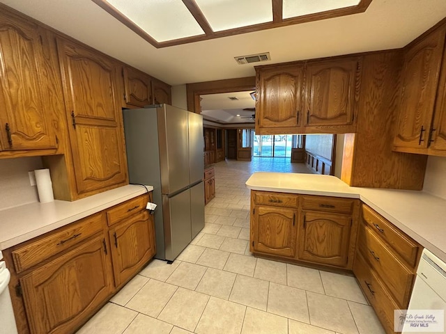 kitchen featuring light tile patterned floors, white dishwasher, stainless steel refrigerator, and kitchen peninsula