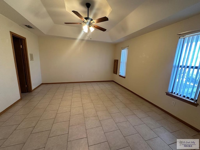 empty room with light tile patterned floors, a raised ceiling, and ceiling fan