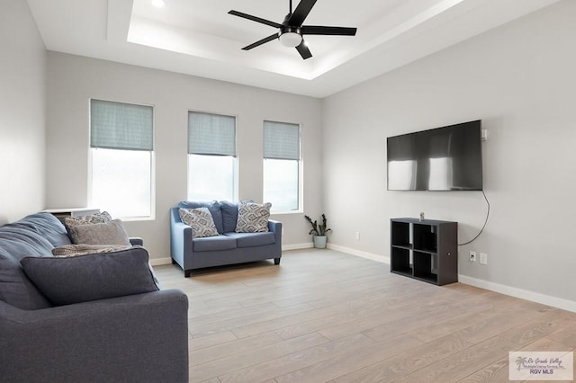 living room featuring light hardwood / wood-style floors, ceiling fan, and a tray ceiling